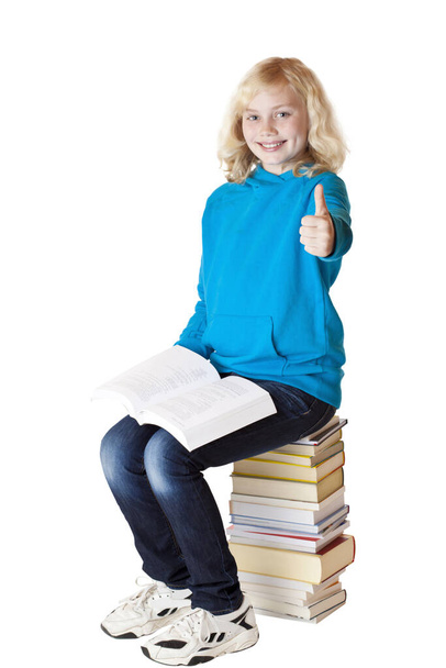 blonde,pretty young schoolgirl sits on stack of books and holds up her thumbs laughing. isolated on white background. - Fotoğraf, Görsel