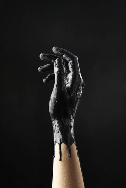 Female refined hand smeared with black acrylic paint on a black background - Zdjęcie, obraz
