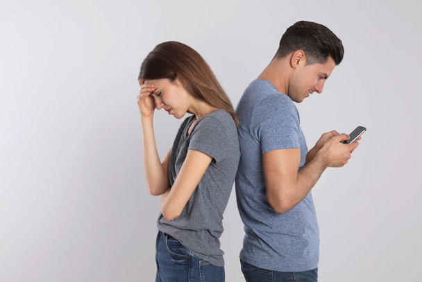 Man with smartphone ignoring his girlfriend on light background. Relationship problems - Фото, изображение