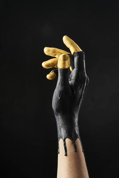 Female refined hand smeared with black and gold acrylic paint on a black background - 写真・画像