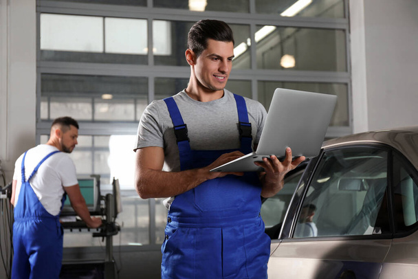 Mechanic with laptop doing car diagnostic at automobile repair  - Foto, Imagen