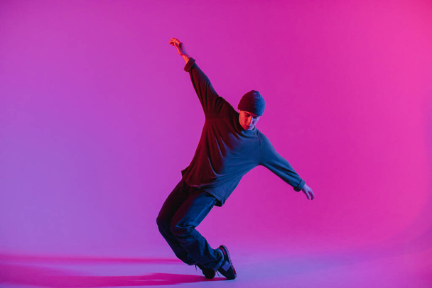 Young Man in a Jumper Dancing Contemporary Dance in Studio. Breakdancing. Dance School Poster. Copy Space. Battle competition announcement. Pink and Blue Background. - 写真・画像