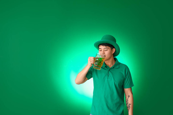 Young Asian man with beer on color background. St. Patrick's Day celebration - 写真・画像