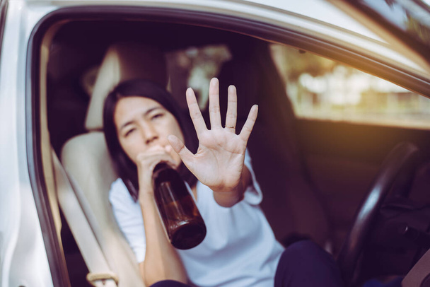 Drunk asian woman drinking alcohol and showing hads stop while driving car on road,Women drive her car with a bottle of beer,Dangerous driving concept - Fotó, kép