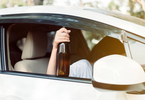 道路上で車を運転しながらアルコールを飲むアジアの女性を飲み、女性はビールのボトルで彼女の車を運転し、危険な運転の概念 - 写真・画像