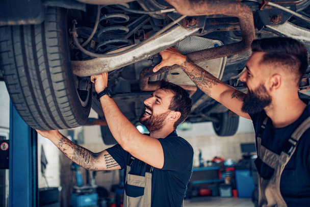 Young mechanics change car wheel in auto repair shop - Фото, изображение