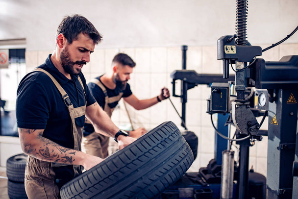 Mecánico trabajando en neumáticos de coche en su tienda
 - Foto, Imagen