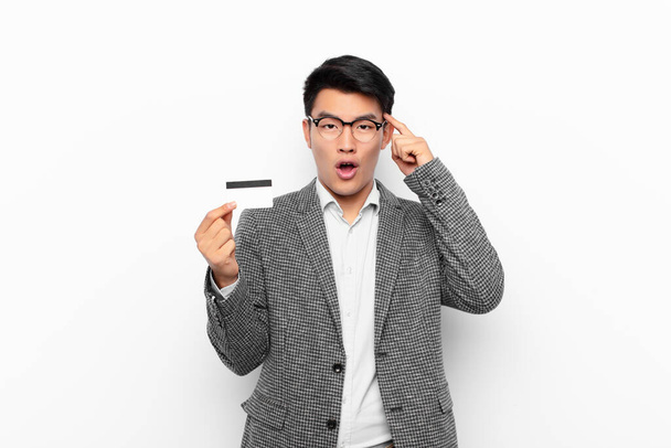young japanese man looking surprised, open-mouthed, shocked, realizing a new thought, idea or concept. credit card concept. - Foto, Imagen