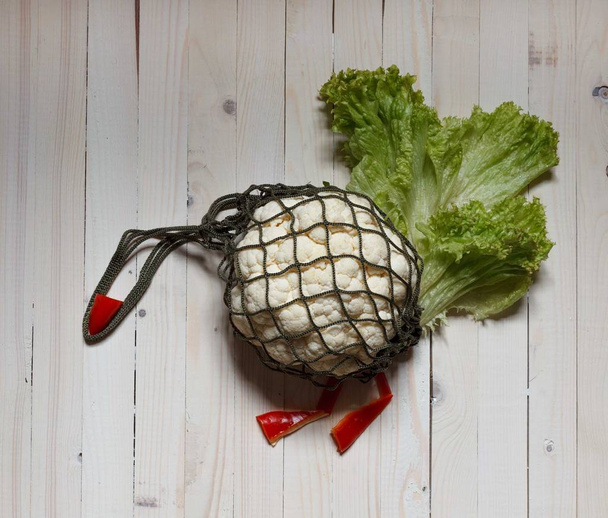 Cauliflower in a string bag, green lettuce and red pepper on a light background, image of a turkey - Fotoğraf, Görsel