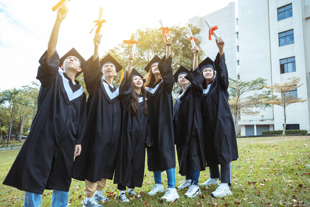 gelukkige studenten in afstudeerjurken met diploma 's op de universiteitscampus - Foto, afbeelding
