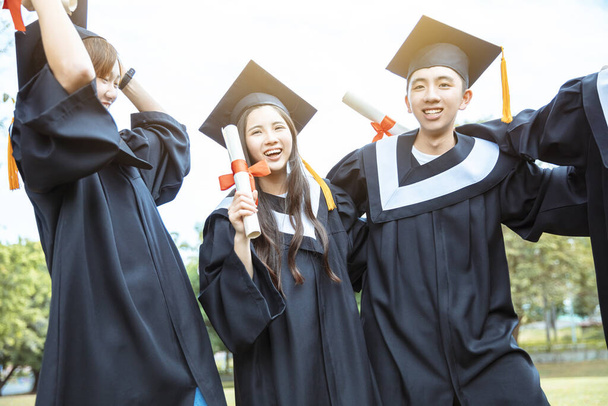 ευτυχείς φοιτητές στην αποφοίτηση φορέματα κατέχουν διπλώματα στην πανεπιστημιούπολη - Φωτογραφία, εικόνα
