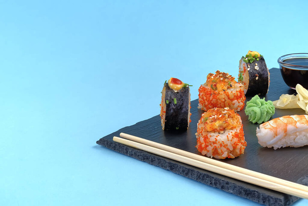 tradicional conjunto de sushi japonés con servicio de piedra negra. sabroso conjunto de sushi, nigiri, sahimi y maki. deliciosa cena o almuerzo para una persona. aislado en azul
 - Foto, Imagen