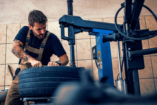 Mecánico trabajando en neumáticos de coche en su tienda
 - Foto, Imagen