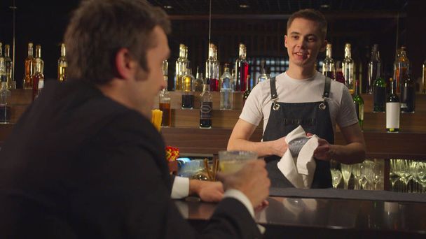 El hombre bebe alcohol y habla con el camarero que limpia un vaso
  - Foto, imagen
