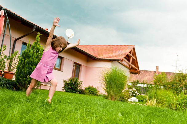 Small girl making cartwheel on garden with family house in background - Foto, imagen