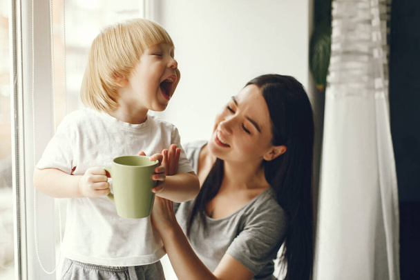 Mother and little son sitting on a windowsill with a tea - Фото, изображение