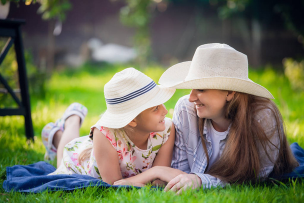 ピクニック中に草の上に横たわる母と小さな娘-空気中の愛、親密さの瞬間に彼女の背中に女の子と女性. - 写真・画像