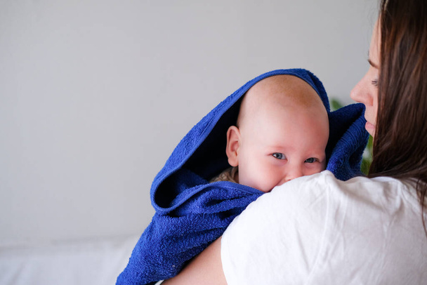 Mom hugs her little cutest baby after bath with blue towel on head. Infant child on mother hands. Mothercare love. Family life. Mother and baby. Happy motherhood - Photo, image