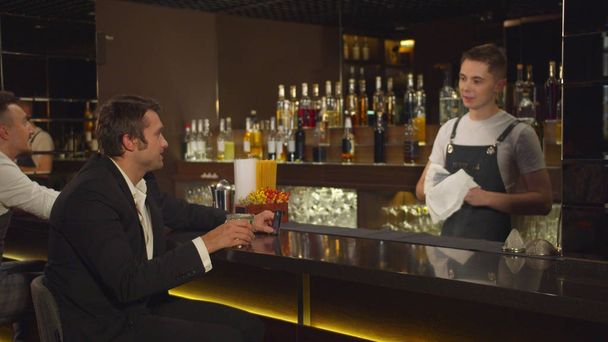 Чоловік сидить у барі, розмовляє з барменом і крутить свою кредитну картку
 - Фото, зображення
