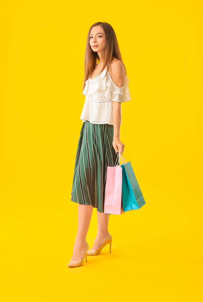 Beautiful young woman with shopping bags on color background - 写真・画像