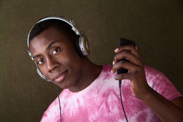 Knappe zwarte man in roze tie-dye shirt verwijdert een deel van zijn hoofdtelefoon - Foto, afbeelding