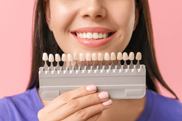 Beautiful young woman with teeth color samples on color background, closeup - 写真・画像