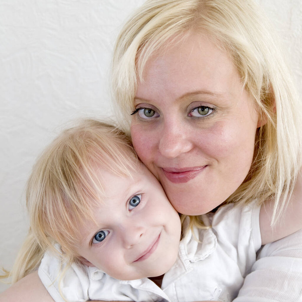 head portrait of a young blond mother with blond four year old daughter with sides touching faces - Photo, image