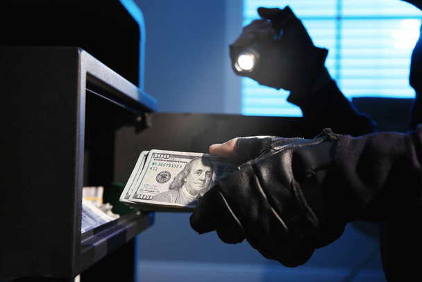 Thief taking money out of steel safe indoors at night, closeup - Photo, image