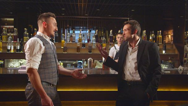 Два чоловіки стоять біля бару і розмовляють один з одним агресивно
 - Фото, зображення