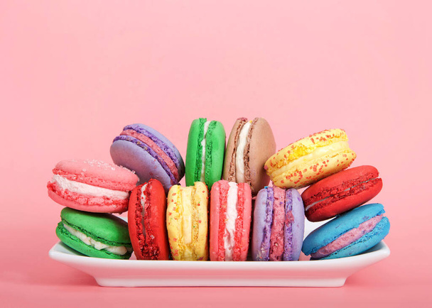 Nahaufnahme auf Macaron-Keksen in verschiedenen Frühlingsfarben gestapelt auf einem weißen Teller auf rosa Hintergrund. beliebter französischer Leckerbissen. - Foto, Bild