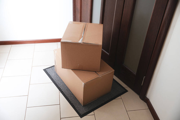 Cardboard boxes on rug near door. Parcel delivery service - Foto, Imagen