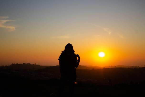 verlicht silhouet van jonge vrouw poseren in zonsondergang van blauwe en rode hemel - Foto, afbeelding