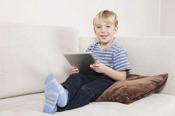 Boy holding tablet PC on sofa - Foto, afbeelding