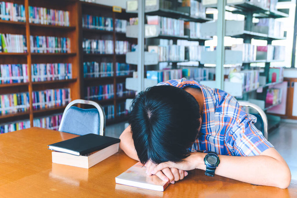 Уставший азиатский студент спит за столом в библиотеке
 - Фото, изображение