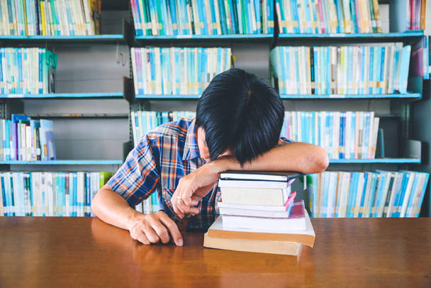 Tired asian student sleeping at the desk in a library - Фото, изображение