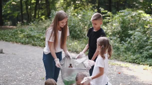 Grupa dzieciaków w rękawiczkach zbierających śmieci w parku miejskim - Materiał filmowy, wideo