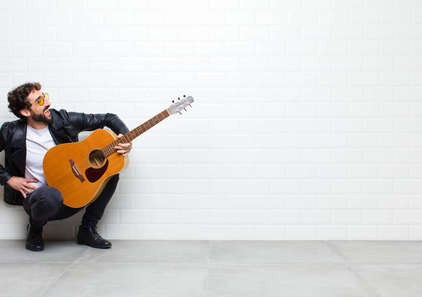 young man with guitar on brick wall background - Valokuva, kuva