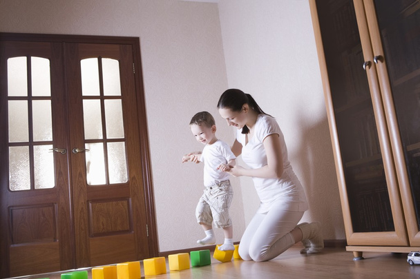 Boy walks along building blocks with help from his mother - Foto, Bild