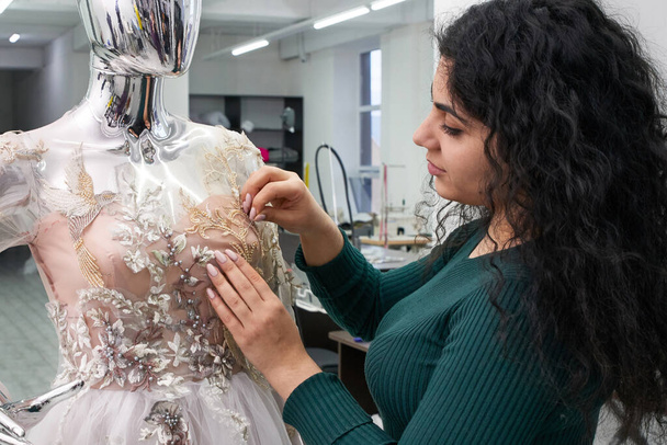 Dressmaker fixing white lace wedding dress on a mannequin in tailor studio - Photo, image