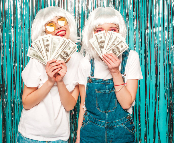 Two young sexy hipster girls in white wigs and red lips.Beautiful trendy women in summer clothes.Carefree models posing on blue silver shiny tinsel background in studio.Positive female having fun - Φωτογραφία, εικόνα