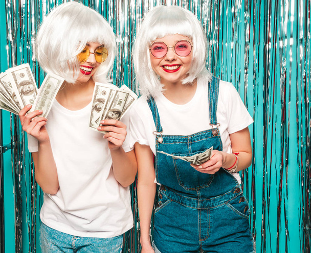 Two young sexy hipster girls in white wigs and red lips.Beautiful trendy women in summer clothes.Carefree models posing on blue silver shiny tinsel background in studio.Positive female having fun - Valokuva, kuva
