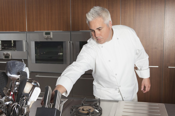 Mid adult chef leans for knife - Фото, изображение