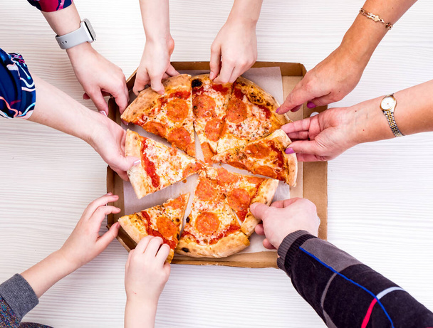 Wszyscy kochają pizzę. Close-up widok z góry młodych ludzi wybierając plastry pizzy podczas lunchu w pomieszczeniach. - Zdjęcie, obraz