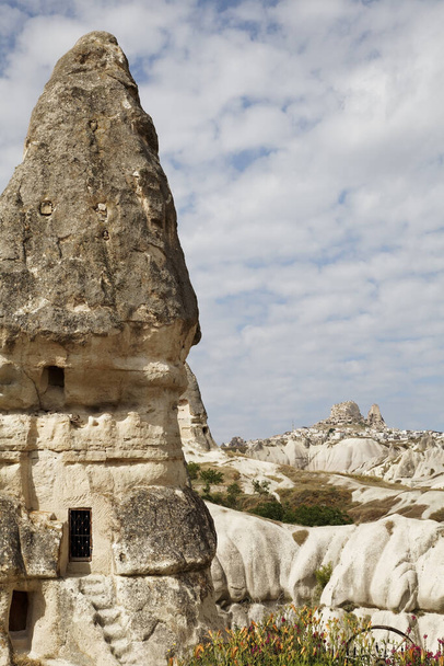 Fairy chimney home made from carving limestone, steps to the path, garden with flower beds and cart wheel ornament, portrait, cloudy sky, copy space, crop area, architectural detail - Φωτογραφία, εικόνα