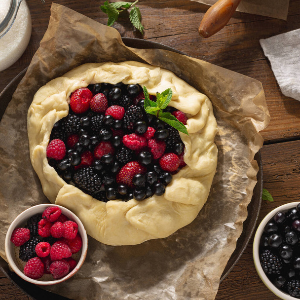 Raw berry pie on wooden table Cooking a pie with raspberries, blueberries and blackberries Top view - Photo, image