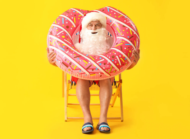 Άγιος Βασίλης με δαχτυλίδι κολύμβησης κάθεται στην ξαπλώστρα με φόντο το χρώμα. Έννοια των διακοπών - Φωτογραφία, εικόνα