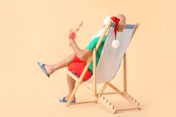 Weihnachtsmann sitzt auf einer Sonnenliege vor farbigem Hintergrund. Urlaubskonzept - Foto, Bild
