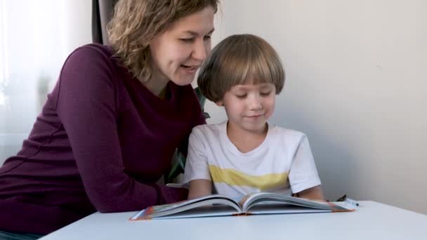 Prechool boy, child, sitting at the table at home and reading with his mom - Záběry, video