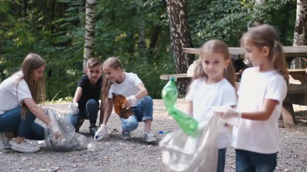 Group of children with young volunteer picking up rubbish in forest - Footage, Video