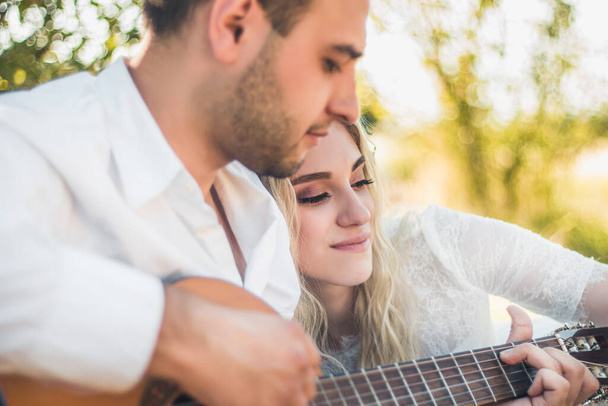 Lovely couple spend free time together, have date, enjoys peaceful atmosphere outdoor in meadow. Romantic guy plays guitar and sing songs to his girlfriend, great love concept - Photo, Image